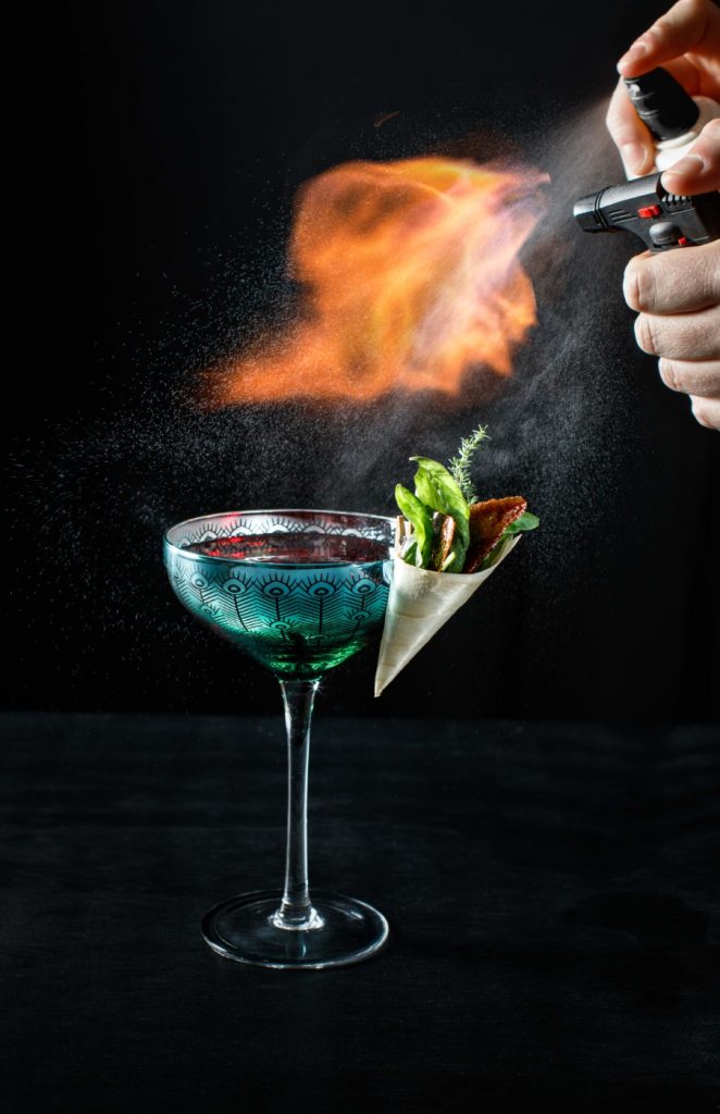 A hand holding a lighter over a glass with a drink.