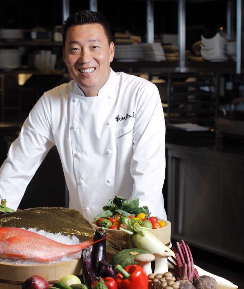 A chef standing behind a table of food.