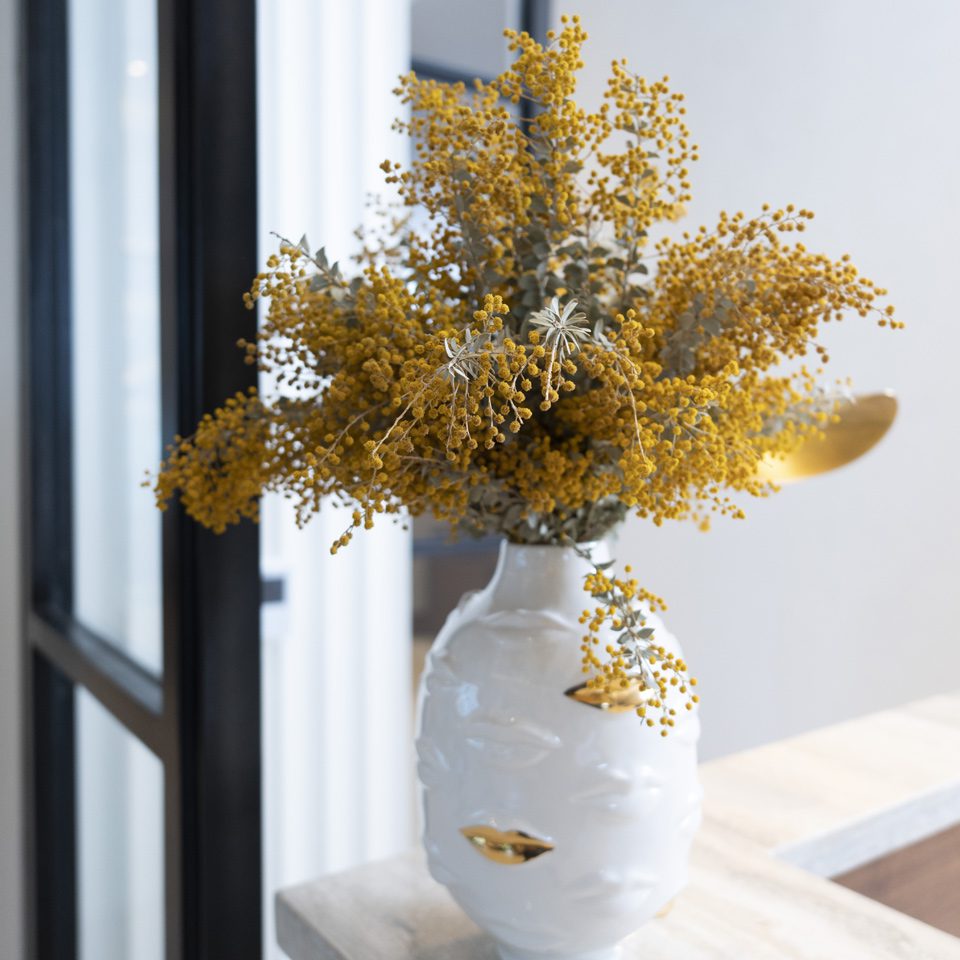A white vase with yellow flowers on top of a table.