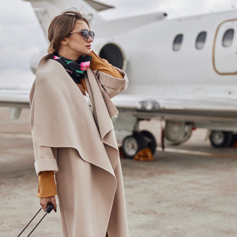 A woman in a beige coat standing next to an airplane.