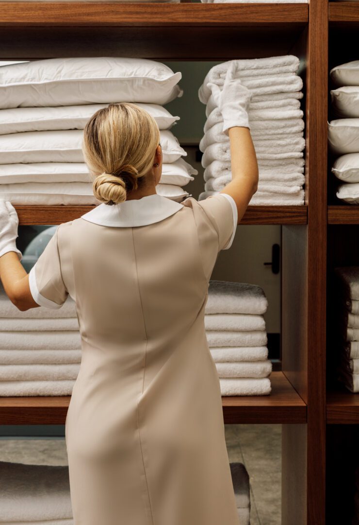 A woman in white dress and gloves standing next to shelves.