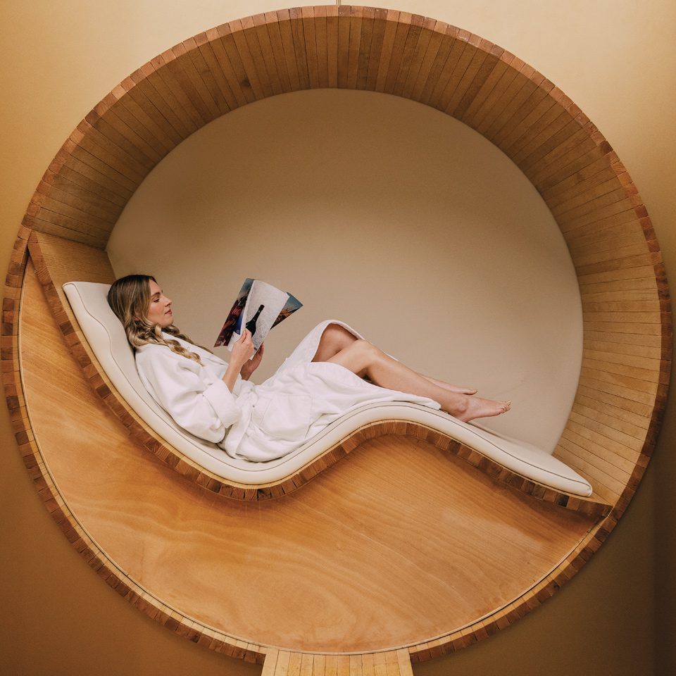 A woman reading in a circular wooden chair.