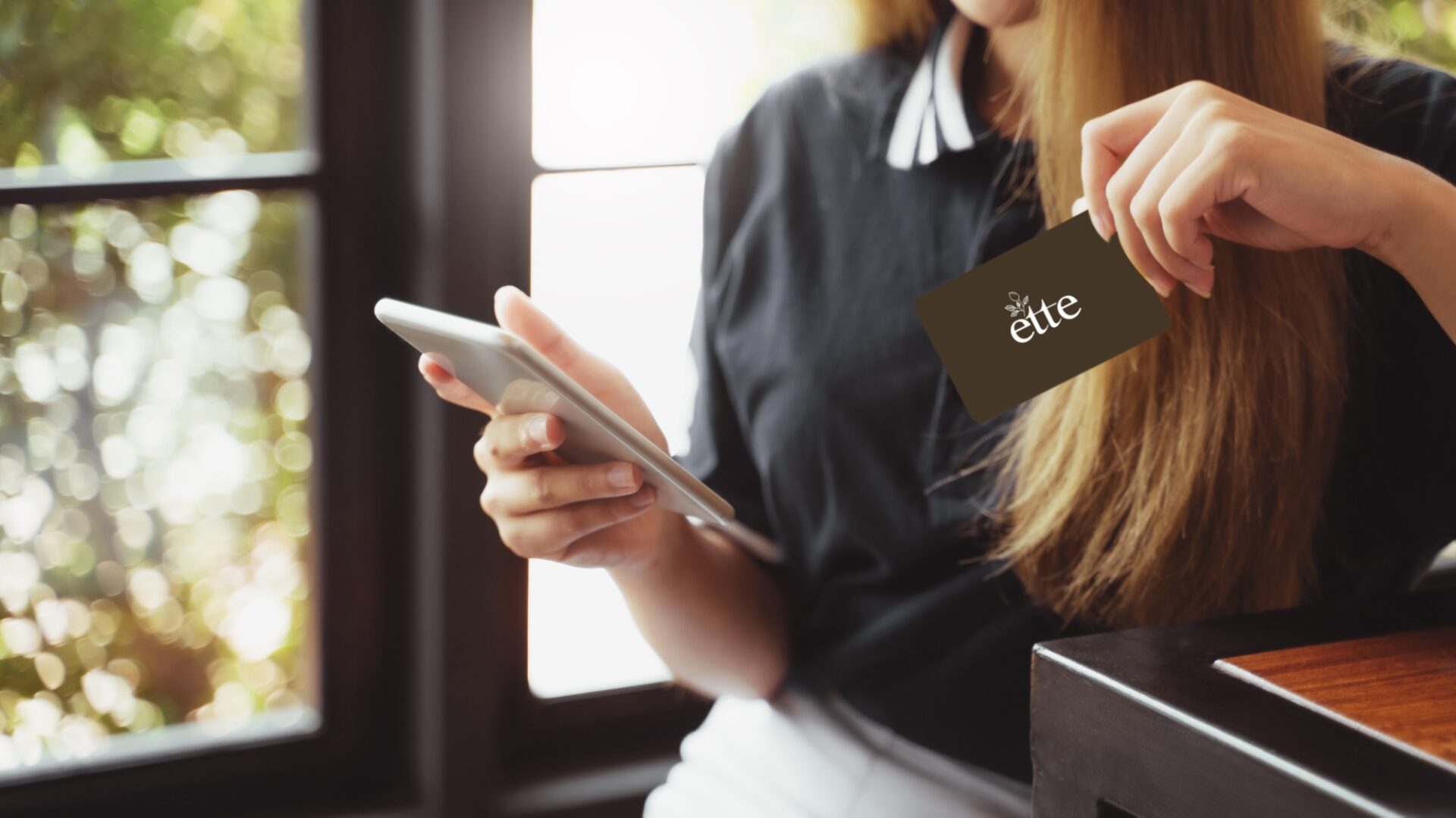 A girl holding an ette logo card watching at the phone