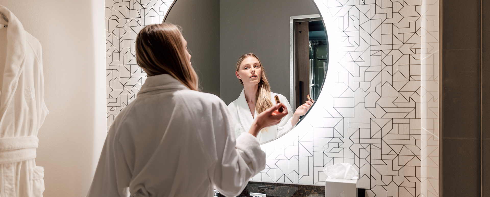 Guest in a robe at the round lit vanity mirror in the Elegant Queen room at ette hotel