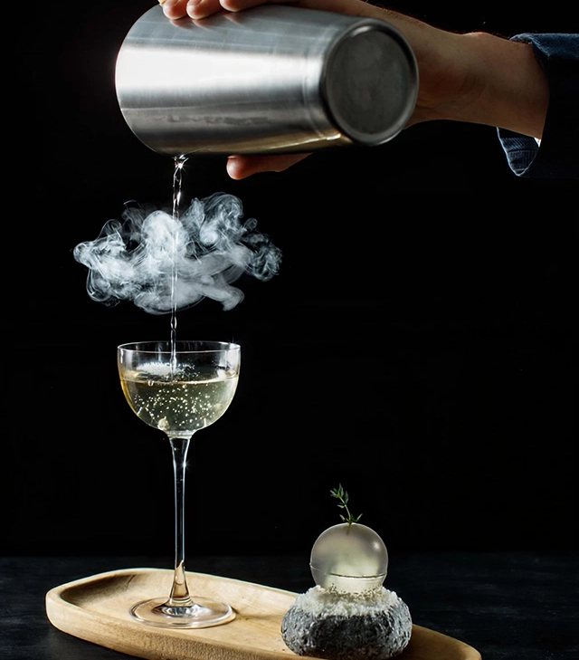Bartender pouring a smoking cocktail into a coupe glass